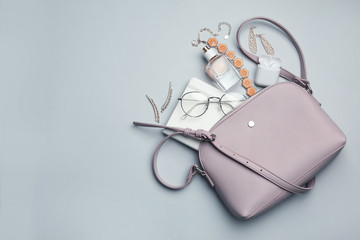 Stylish woman's bag with accessories on light grey background, flat lay. Space for text