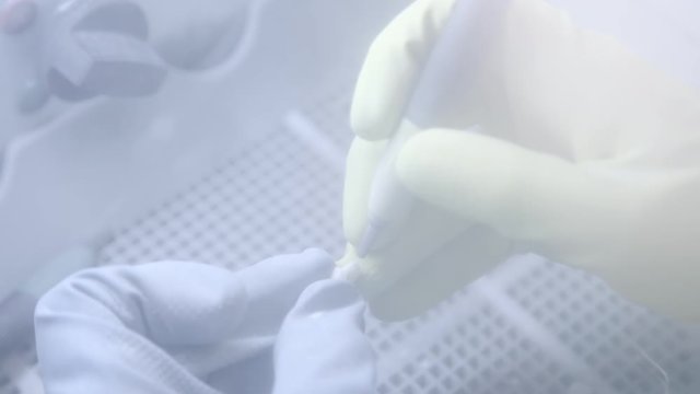 Dental technician polishing artificial ceramic teeth using sandblaster in the dental lab. Professional wearing gloves while holding fake teeth in hand and polishing it with sand blaster