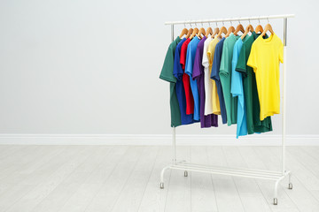 Rack with colorful t-shirts in room. Space for text