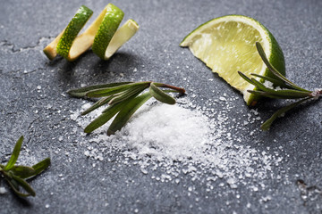 Slices of fresh lime, salt and rosemary dark concrete background. Copy space. Ingredients for...