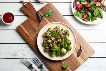 Delicious Brussels sprouts with bacon on white wooden table, flat lay