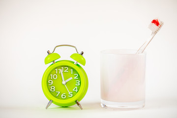 A photo of the green alarm clock and toothbrush. Time to clean the teeth. Dental care, personal hygiene concept photo. An important reminder for children and grown ups to take care of their teeth.