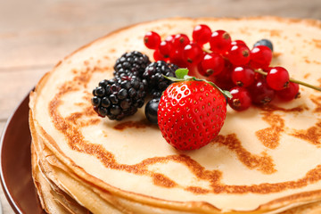 Delicious thin pancakes with berries on plate, closeup
