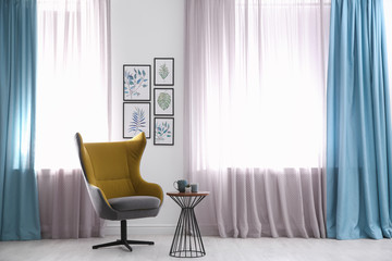 Modern armchair and beautiful paintings of tropical leaves in stylish living room. Interior design