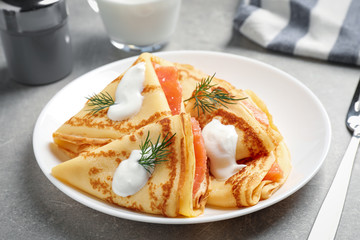 Delicious thin pancakes with salmon and sour cream on light table