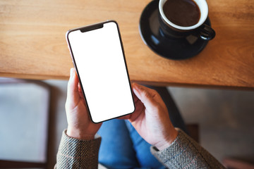 Top view mockup image of a woman holding black mobile phone with blank desktop screen while sitting in cafe