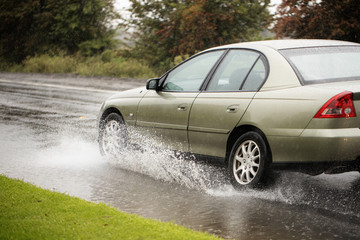 gold car driving through a puddle on a rainy day creating a splash