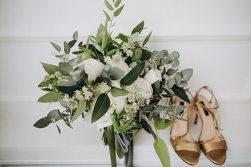 Wedding bouquet of white flowers and greenery is on a white background next to women's heels shoes