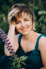 Naklejka premium Beautiful romantic woman blonde in a field of purple flowers lupins smiling with a flower. Soft selective focus.