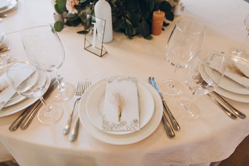 on the festive table there are plates with napkins and name cards, glasses, candles, cutlery are lying, there are compositions of flowers