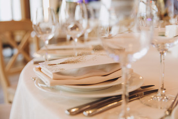on the festive table there are plates with napkins and name cards, glasses, candles, cutlery are lying, there are compositions of flowers