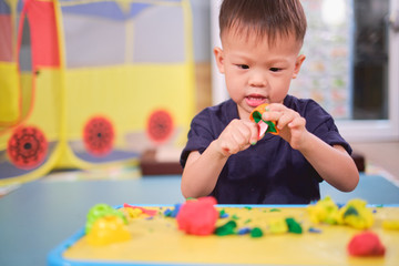 Cute little Asian 2 - 3 years old toddler boy child having fun playing colorful modeling clay /...