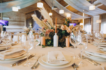on the festive table there are plates with napkins and name cards, glasses, candles, cutlery are lying, there are compositions of flowers