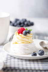 Coffee mug and Pavlova cake with whipped cream and fresh berries on white plate. Scandinavian style. Soft focus