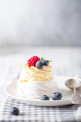 Delicious Pavlova cake with whipped cream and fresh berries on white plate. Scandinavian style. Soft focus