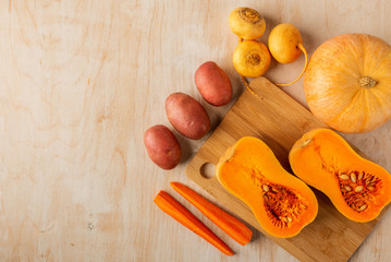 pumpkin halves on a bamboo cutting Board and other vegetables on a light wooden background