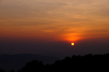 Gorgeous view of sunset with mountain range for background and silhouette of forest as foreground.