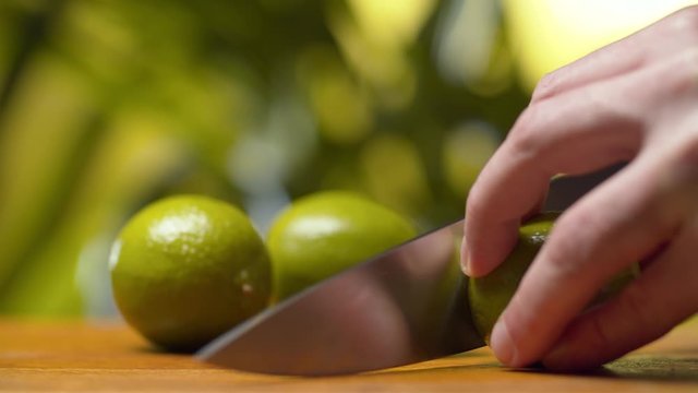 Close up male hand cutting a lime on green natural background. Making drinks. Healthy lifestyle and eating concept.