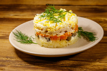 Tasty layered salad with potatoes, chicken breast, marinated mushrooms, carrots, eggs and mayonnaise on wooden table