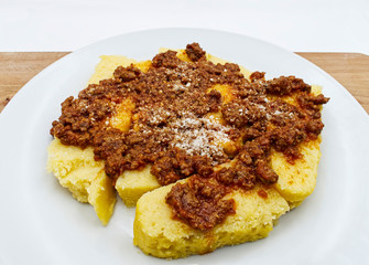 Polenta with bolognese sauce and parmesan cheese on wooden table