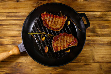 Grilled pork steaks with rosemary, garlic and spices in cast iron grill frying pan on wooden table....