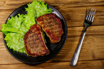 Grilled pork steaks with lettuce leaves on wooden table. Top view