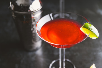 Red cocktail with lime in Martini glass on a table.