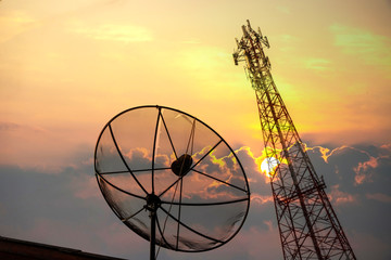 Communications satellite dish and a telecommunications tower at the sunset