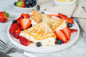Close up Thin crepes with ricotta cheese and fresh strawberries on a gray concrete background.