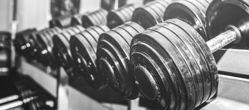 Heavy dumbbells lying in the raw in the gym. Fitness sport motivation. Happy healthy lifestyle living. Exercises with bars weights. Black and white photo.