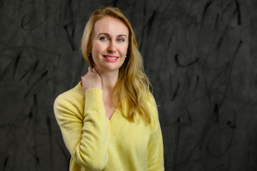 Fototapeta premium Portrait of a stylish business pretty blonde woman in a yellow sweater on a gray background
