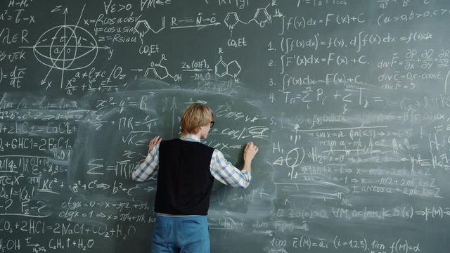 Crazy young man beating chalkboard yelling feeling angry because of science problem writing formulas. Education and negative emotions concept.