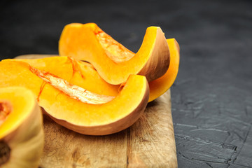 Pumpkin, butternut squash pieces on wooden cutting board on black background, closeup. Cooking winter squash, food ingredient