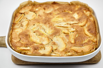 Apple pie, dessert from stewed fruits in ceramic dish for baking in the oven . Charlotte on wooden cutting board on white background