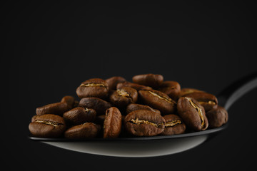 coffee beans in black spoon, fresh roast. black background