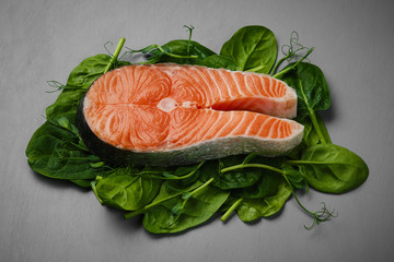 Salmon steak raw fish on spinach leaf and microgreens,  prepared for cooking. top view. grey background