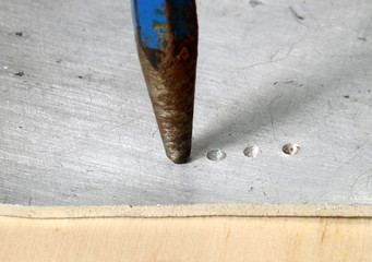 Close up on a blue ceter punch in use for placing marks on a piece of metal.