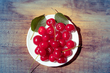 Ripe cherries on a white plate on a wooden table