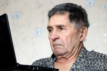 Elderly man using laptop, male looks at the notebook screen intently. Concept of online...