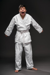 a teenager dressed in martial arts clothing posing and crying on a dark gray background, a sports concept