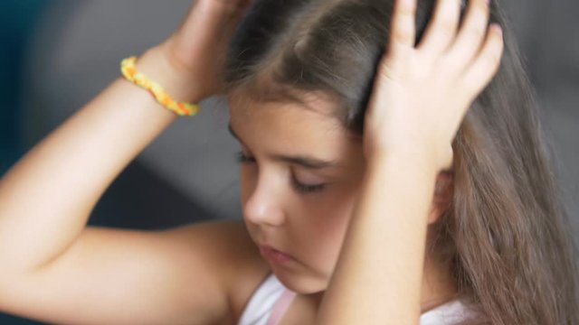 Little child girl collects her hair in a ponytail. Pulls the ponytail with a hair band. Wear a headband. Girl does her hair. Long beautiful curly hair. Close up