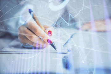 Double exposure of woman's hands making notes with forex graph hologram. Concept stock market analysis.