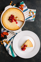 Freshly baked homemade cottage cheese pie with dried apricots, almonds and raspberries. A piece on a white plate decorated with berries and Cutlery top View on a dark background