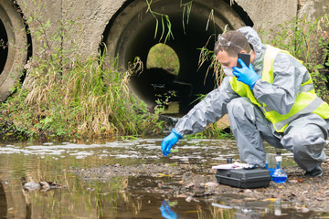 a man in protective gloves and a mask makes a quick analysis of water from the river for pollution...