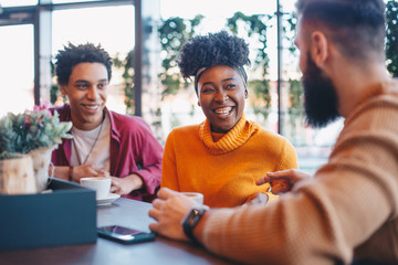 Two guys and a girl sitting in a cafe, talking. The girl is smiling.