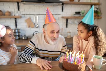 Bearded man in a birthday hat having his birthday with his granddaughters