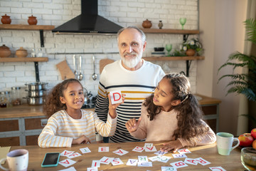 Two dark-skinned girls spending time with their granddad and looking pleased