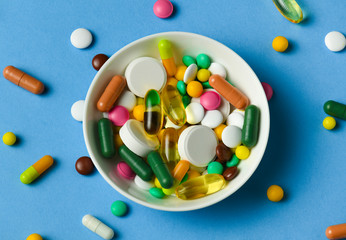 A dish full of pills, tablets, vitamins, drugs, omega 3 fish oil, gel capsules, medicament and food supplement for health care. Blue background. © soleg