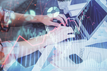 Double exposure of stock graph with businessman typing on computer in office on background. Concept of hard work.