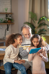 Grey-haired bearded man and his granddaughters watching a video together and smiling